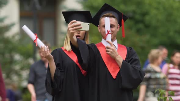 Man and Woman in Academic Dresses Taking Selfie After Graduation Ceremony