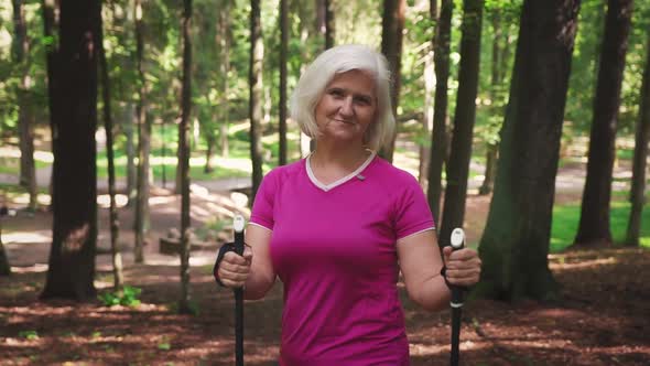 Portrait of an athletic mature woman doing nordic walking in a summer forest.