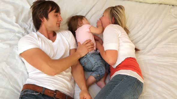 Family with young child playing together on bed