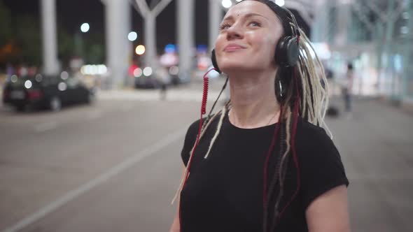 Young Attractive Hipster Woman Use Smartphone Listening Music and Dance on Street at Night