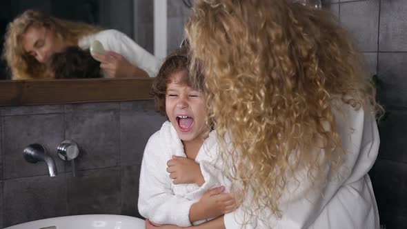 Young Mum in White Coat Combing Her Curly Hair Her Cheerful Five Aged Son in Bathroom