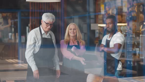 View Through Window of Happy Diverse Waiters Looking at Camera with Hands Crossed in Restaurant