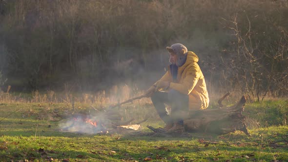 Tourist in Yellow Jacket Near the Fire in the Autumn Forest