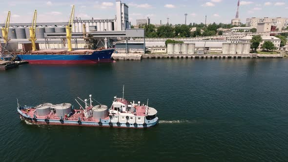 Aerial Shot of a Small Barge Moving Along a River Embankment on a Sunny Day  