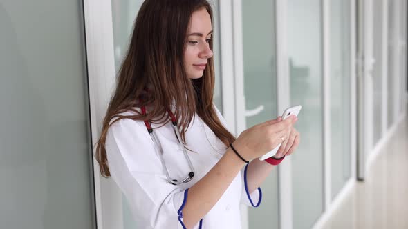 Youg Female Doctor Using Phone During Break in Clicic