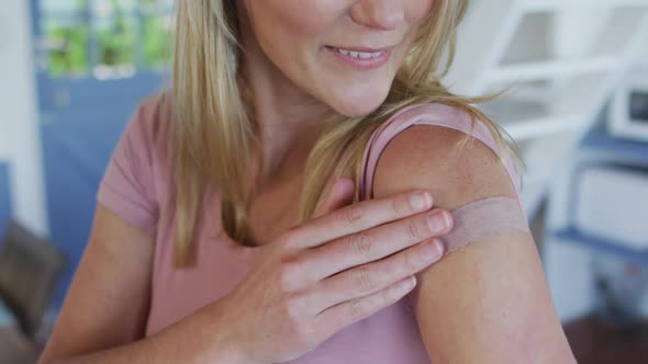 Happy caucasian mature woman showing plaster on arm where she was vaccinated against coronavirus