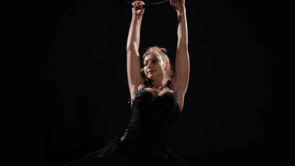 Slim Young Woman Spinning Fast Hanging on Air Hoop at Black Background