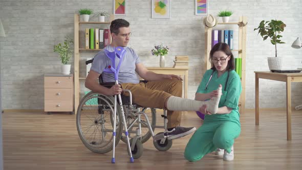 Physiotherapist Examines the Broken Leg of a Man in a Wheelchair After an Injury