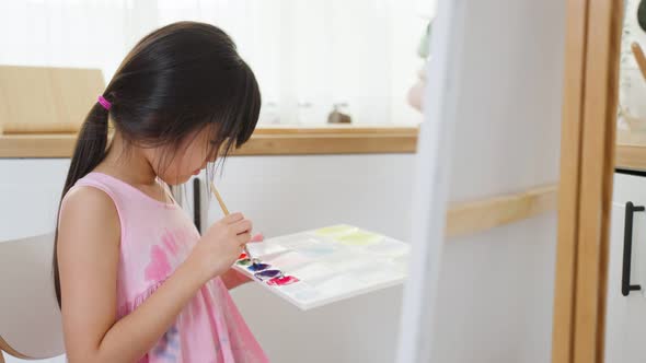 Asian young happy kid girl coloring on painting board in living room.