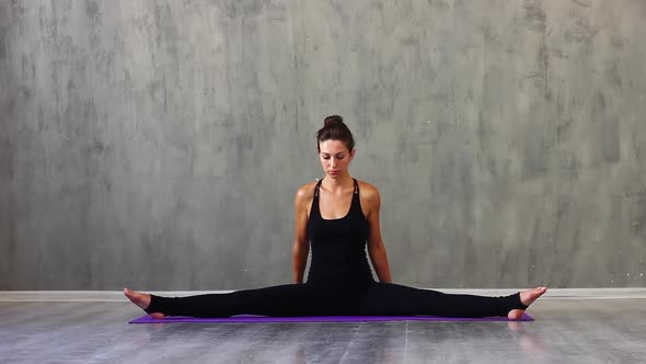 Woman in Sports Purple Yoga Pants Sitting on Shapagata Doing Stretching with Her Hands