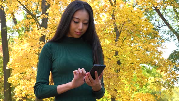 A Young Asian Woman Works on A Smartphone in A Park