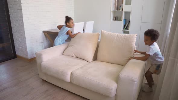 Happy Boy and Girl Children Playing Running Round Couch in Home Living Room