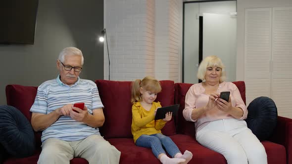 Grandparents and Grandchildren Sit on the Couch at Home and Use Mobile Phones and Digital Tablet