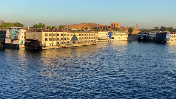 Several cruises docked on the banks of the Nile River where there is a famous temple at sunset. Conc
