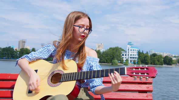 A Woman Is Playing the Acoustic Guitar Outdoors