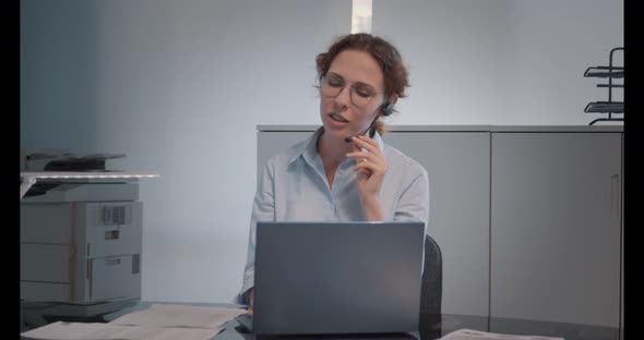 Female Operator in Braces and Headset Talking with Costumer Working on Laptop Computer in Office