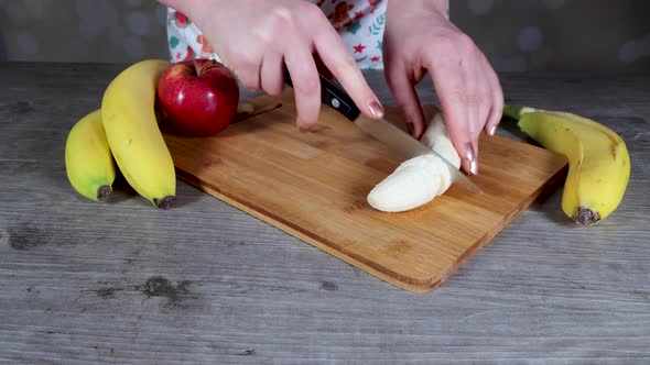 A woman in a kitchen cutting up a banana on a chopping board