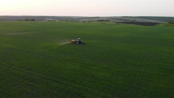 Aerial View of Farming Tractor Spraying on Field with Sprayer, Herbicides and Pesticides at Sunset