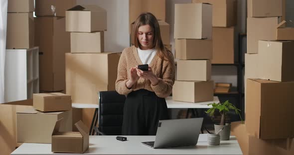 Female Business Owner Is Checking Email in Smartphone in Domestic Warehouse Standing Between