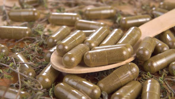 Full wooden spoon of medical herbal capsules in a pile of herbs and pills