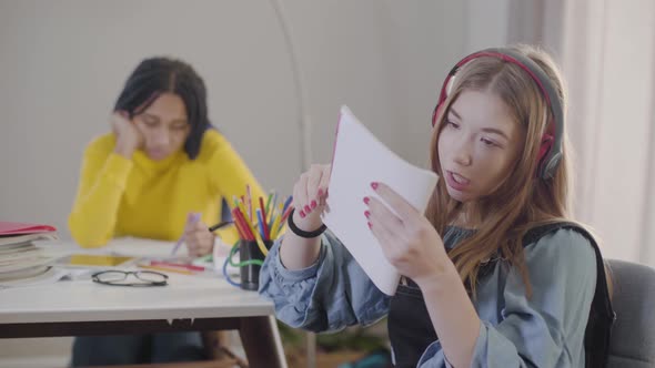 Teenage Caucasian Girl in Earphones Throwing Away Notebook and Singing