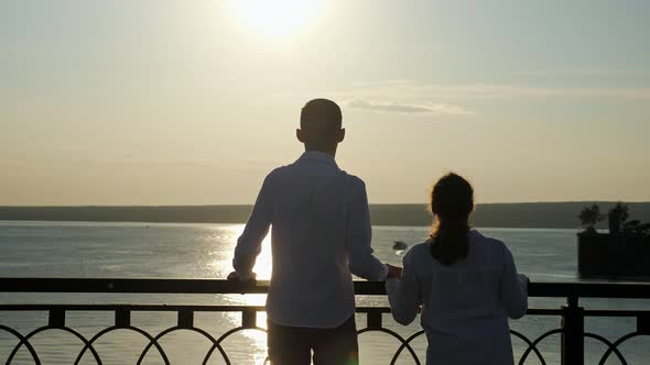 Young Disabled Couple Looks at River at Back Sunset Light