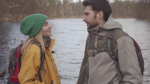 Portrait of the Young Couple of Tourists Standing on the River Bank with Backpacks on Their Backs