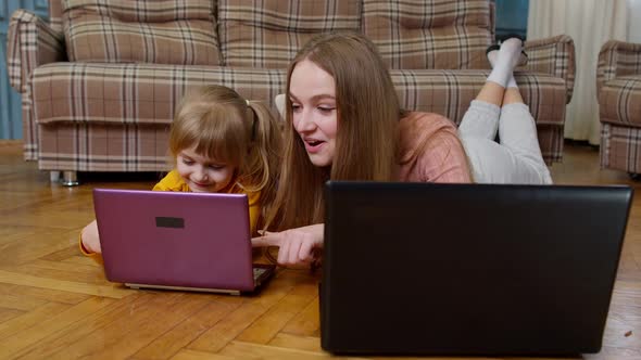 Woman Nanny and Child Girl Studying Together with Computer Laptop While Lying on Warm Floor at Home