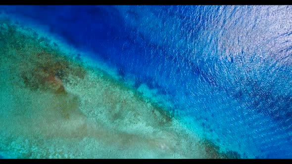 Aerial flying over seascape of tranquil tourist beach vacation by blue green ocean and white sand ba