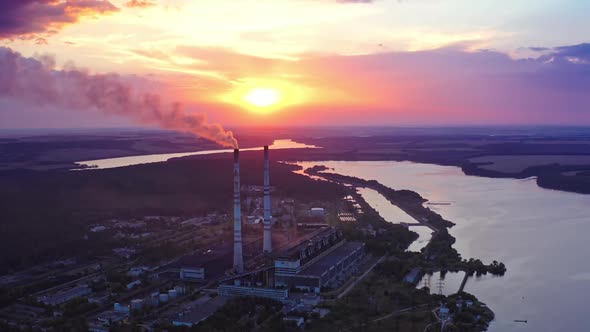 Factory on colorful sky background at sunset. Manufacturing near the river. Aerial view.