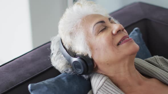 Close up of african american senior woman wearing headphones listening to music sitting on the couch