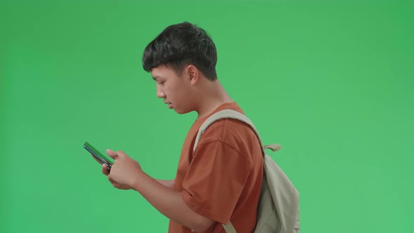 The Side View Of Asian Boy Student Using Mobile Phone While Walking To School On Green Screen