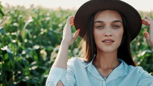 Portrait of Beautiful Young Girl in Hat Standing at a Corn Field Smiling and Looking at Camera