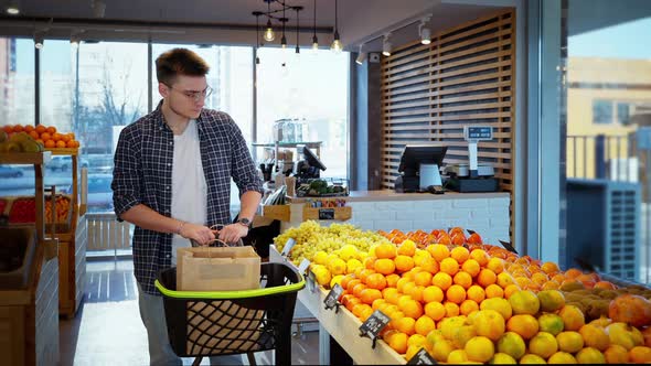 Man is Shopping in Organic Food Shop Choosing Lemon in Showcase with Citrus Fruits