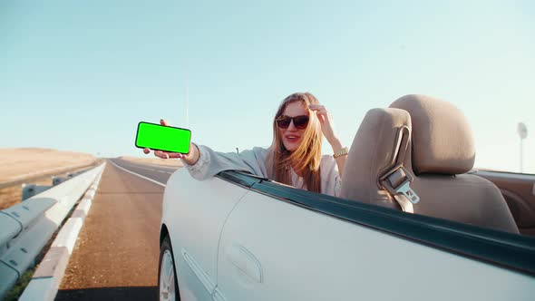 A Woman with Glasses on a Convertible Shows Her Phone and Smiles