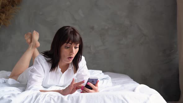 Caucasian Woman Lying in the Bedroom on the Bed with the Phone Chatting Online Makes Purchases
