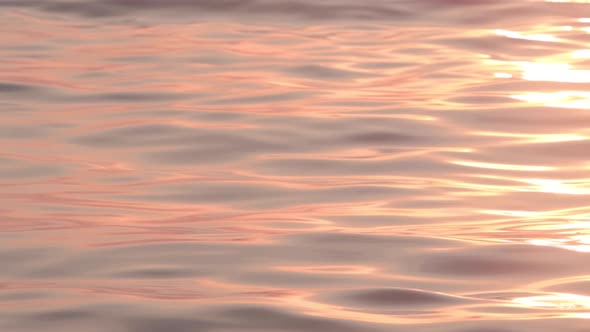 Orange sunlight glimmering on slowing smooth ripples and waves