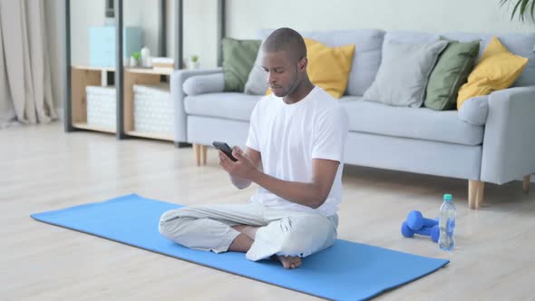 Young African Man Using Smartphone on Yoga Mat at Home