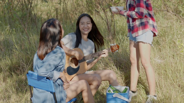 Asian woman happy with friends camping in nature having fun together playing guitar.