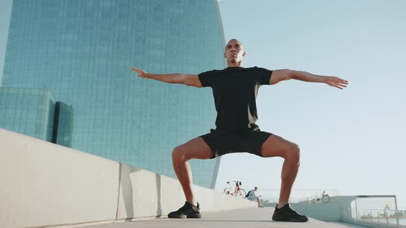 Handsome bald sportsman wearing black t-shirt bends to the side outdoors