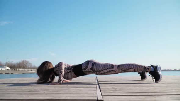 fit girl in leggings, black sneakers does sport exercises against blue lake