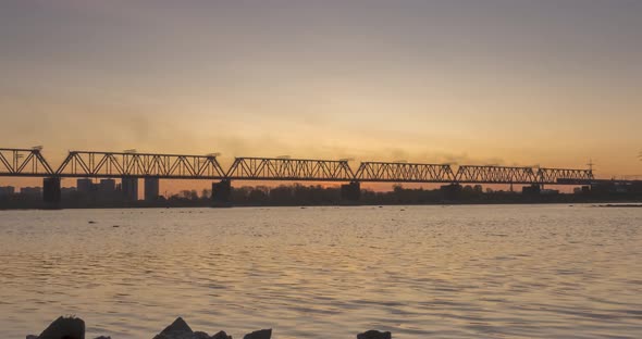 Timelapse of City River Bank. Sun Rays, Blue Sky and Railway Bridge Over Horizont. Summer Sunrise