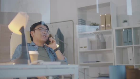 Joyous Asian Man Chatting on Phone at Workplace in Office