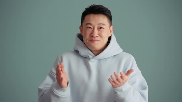 Positively surprised Asian man wearing hoodie clapping hands