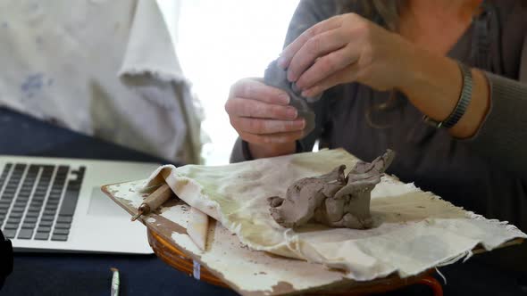 Mature female potter molding a clay while using laptop