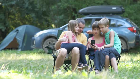 Young Parents with Their Kids Relaxing Together at Camping Site Browsing in Smartphone