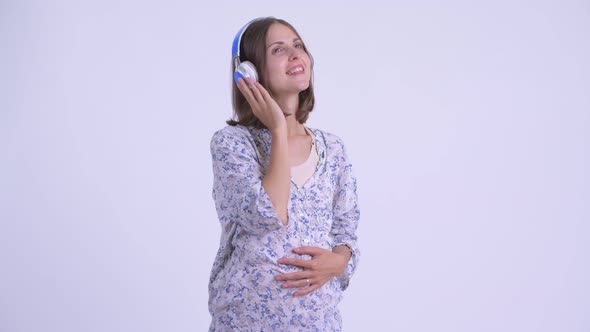 Happy Young Pregnant Woman Thinking While Listening To Music