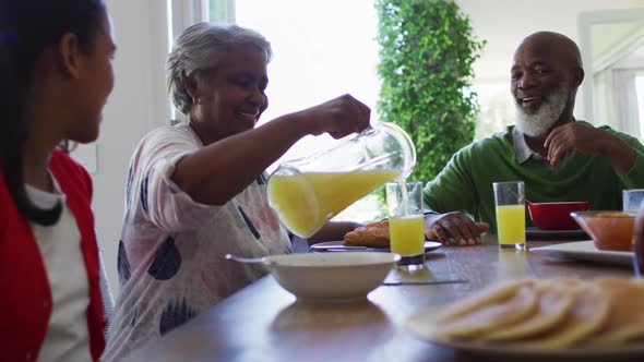 African american grandmother talking to her granddaughter while pouring juice in the glass