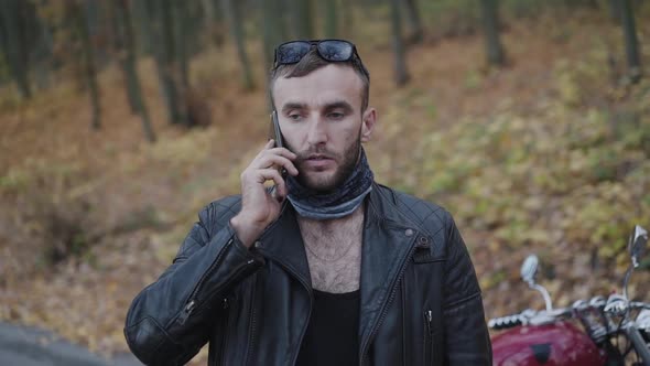 Portrait of Serious Brutal Man in Leather Talking on the Phone in Park