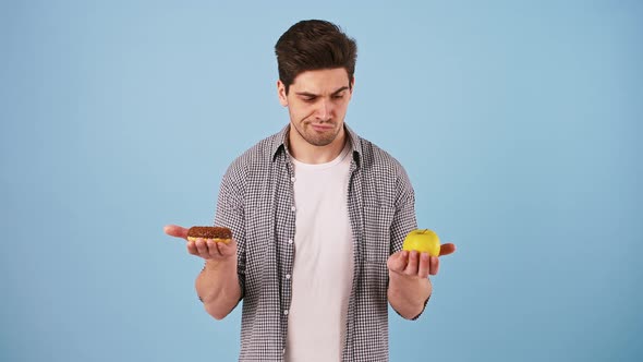 Young Man is Taking Out an Apple and Donut From Behind His Back Licking Lips Thinking What Should He